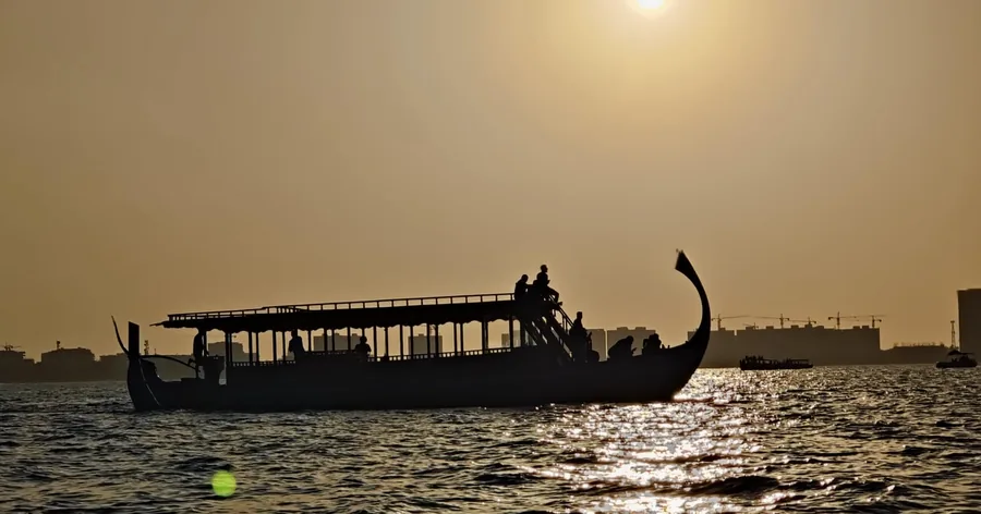 Ein traditionelles dhoni-Boot, das sich als Silhouette auf ruhigem Wasser bei Sonnenuntergang abhebt