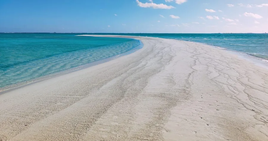 Eine lange, geschwungene Sandbank in einer flachen türkisfarbenen Lagune